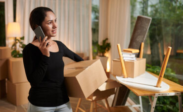Smiling woman packing belonging and ordering movers and van by phone